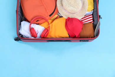 Photo of Travel abroad. Packed suitcase on light blue background, top view. Space for text