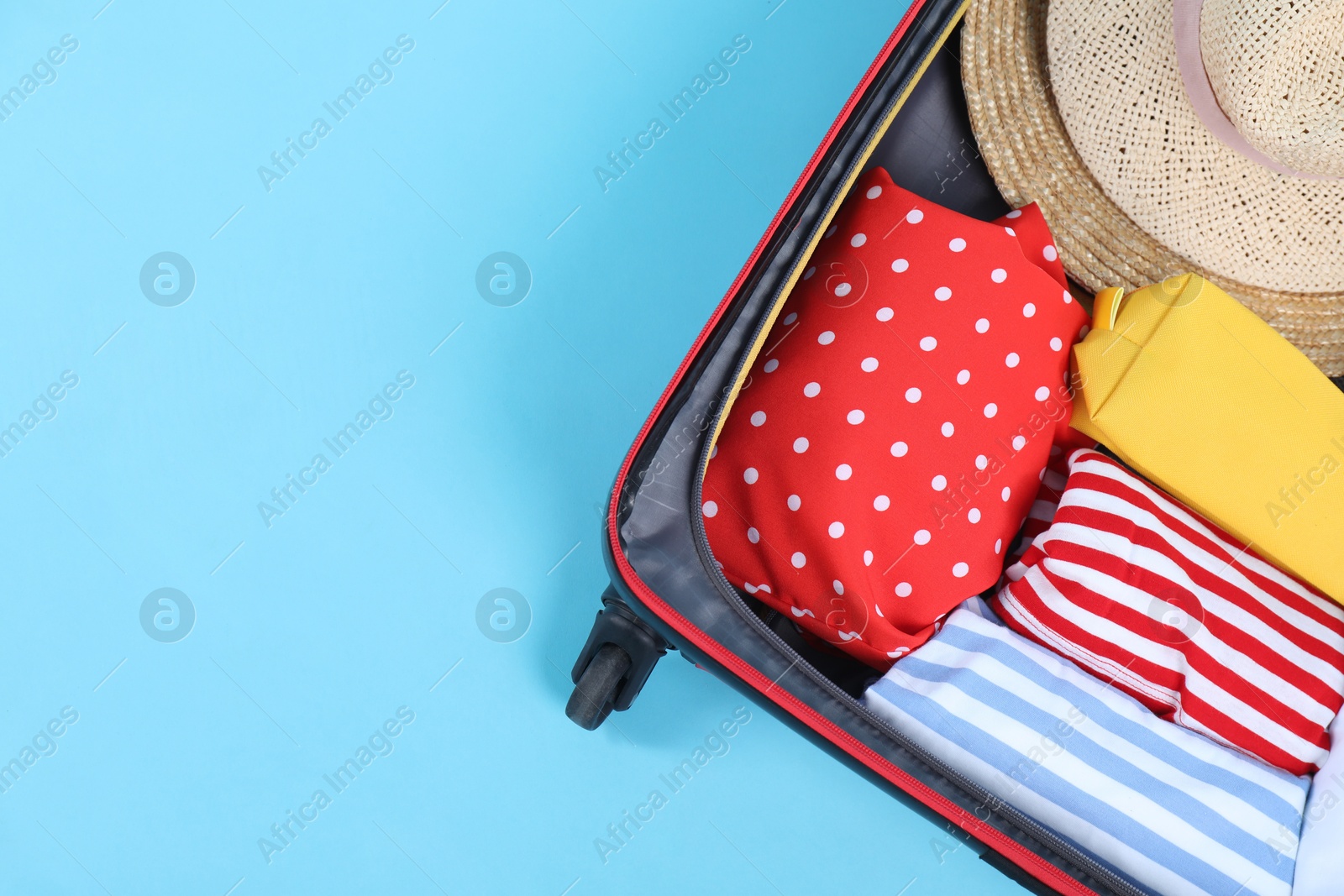 Photo of Travel abroad. Packed suitcase on light blue background, top view. Space for text