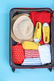 Photo of Travel abroad. Packed suitcase on light blue background, top view