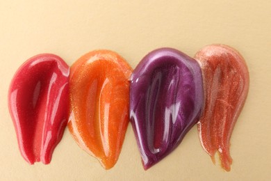 Photo of Samples of different lipglosses on beige background, top view