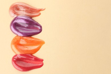 Photo of Samples of different lipglosses on beige background, top view. Space for text