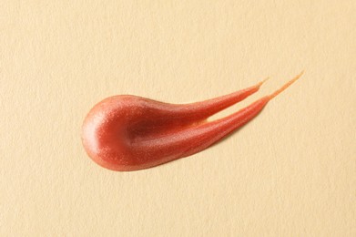 Photo of Sample of orange lipgloss on beige background, top view