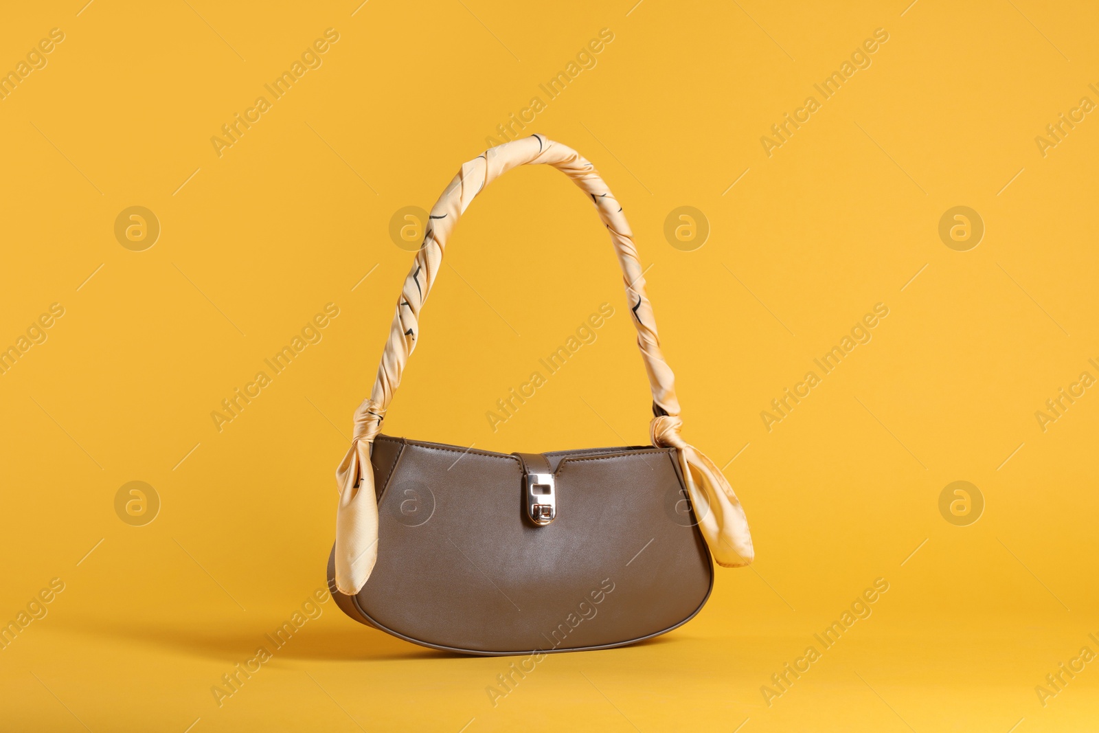 Photo of Stylish brown leather bag with handkerchief on yellow background