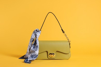 Photo of Stylish leather bag with handkerchief on yellow background