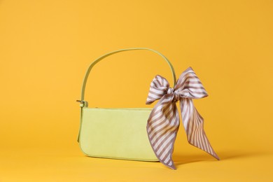 Photo of Stylish light green leather bag with handkerchief on yellow background,