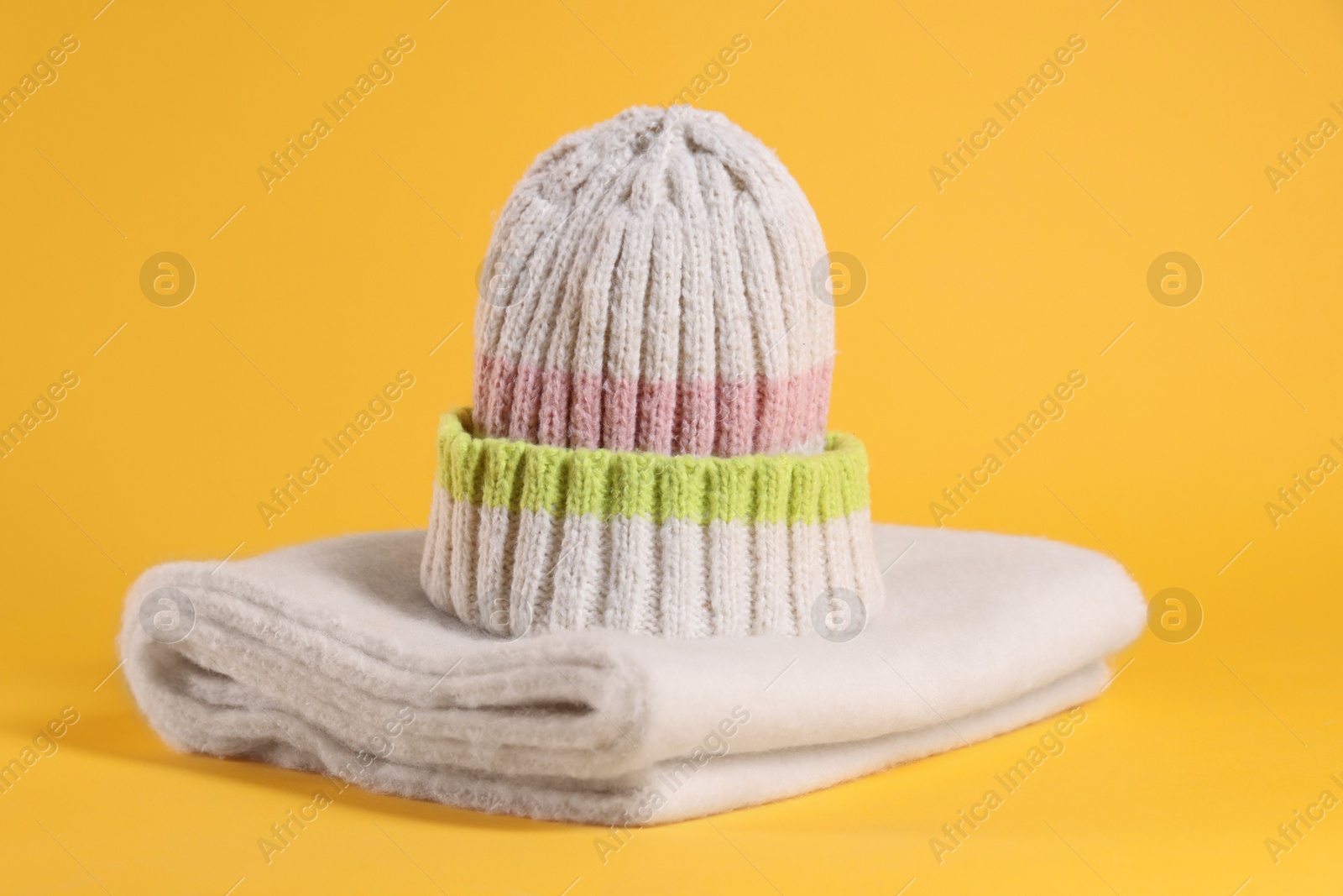 Photo of Stylish knitted hat and warm scarf on yellow background