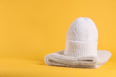 Photo of Stylish knitted hat and warm scarf on yellow background, space for text