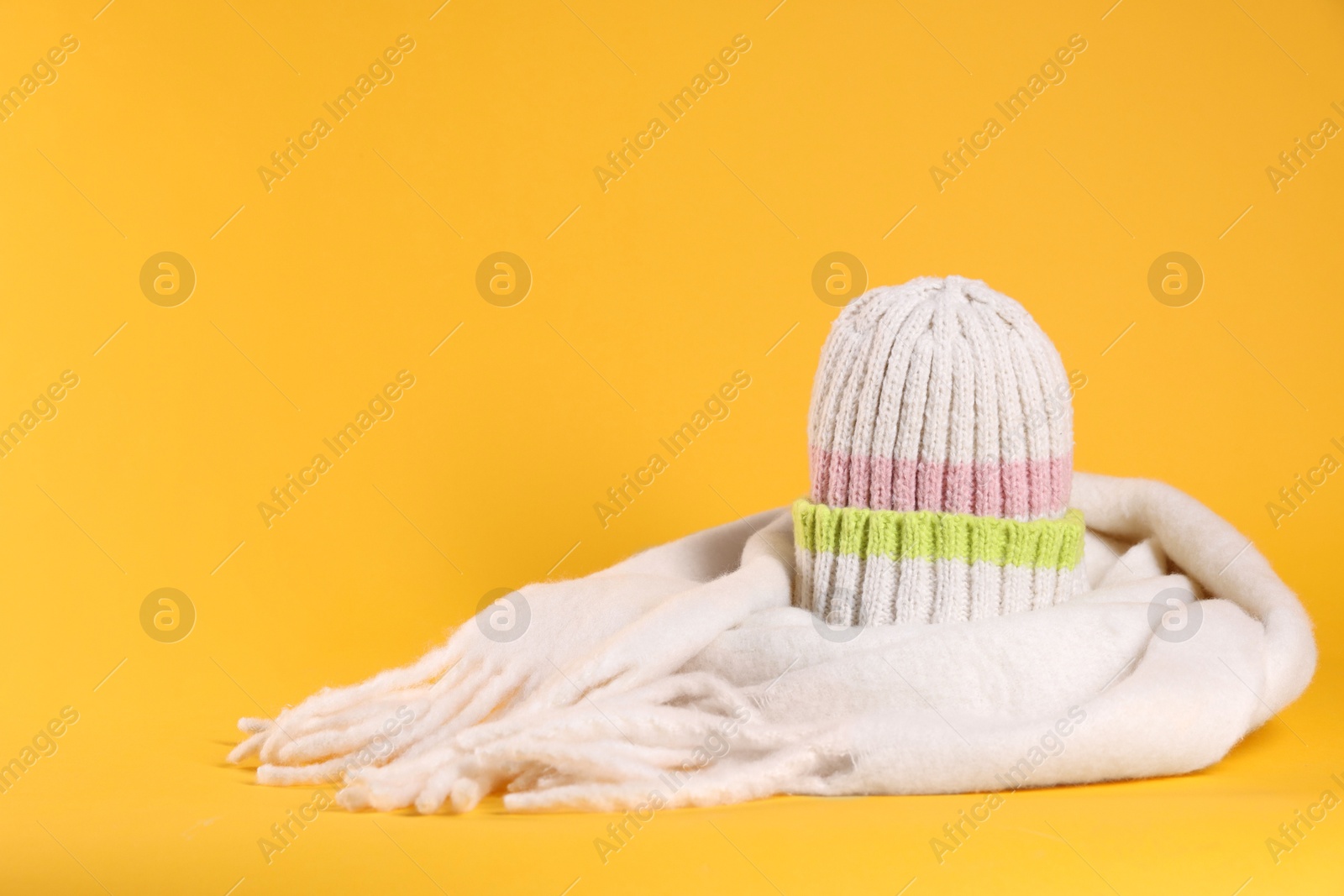 Photo of Stylish knitted hat and warm scarf on yellow background, space for text