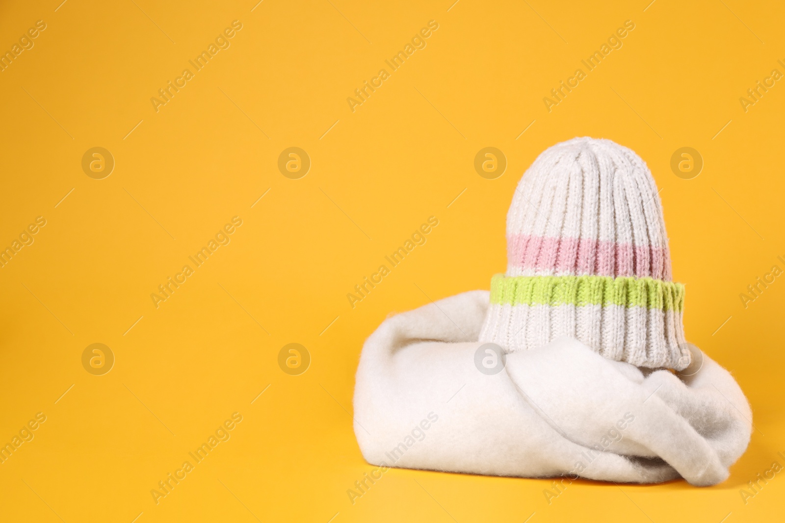 Photo of Stylish knitted hat and warm scarf on yellow background, space for text