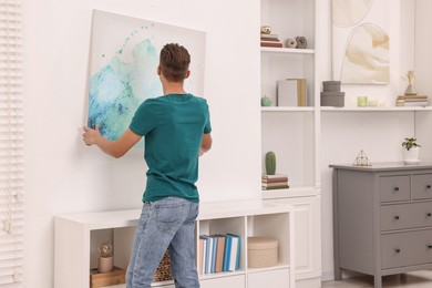 Photo of Decorator hanging abstract picture indoors, back view