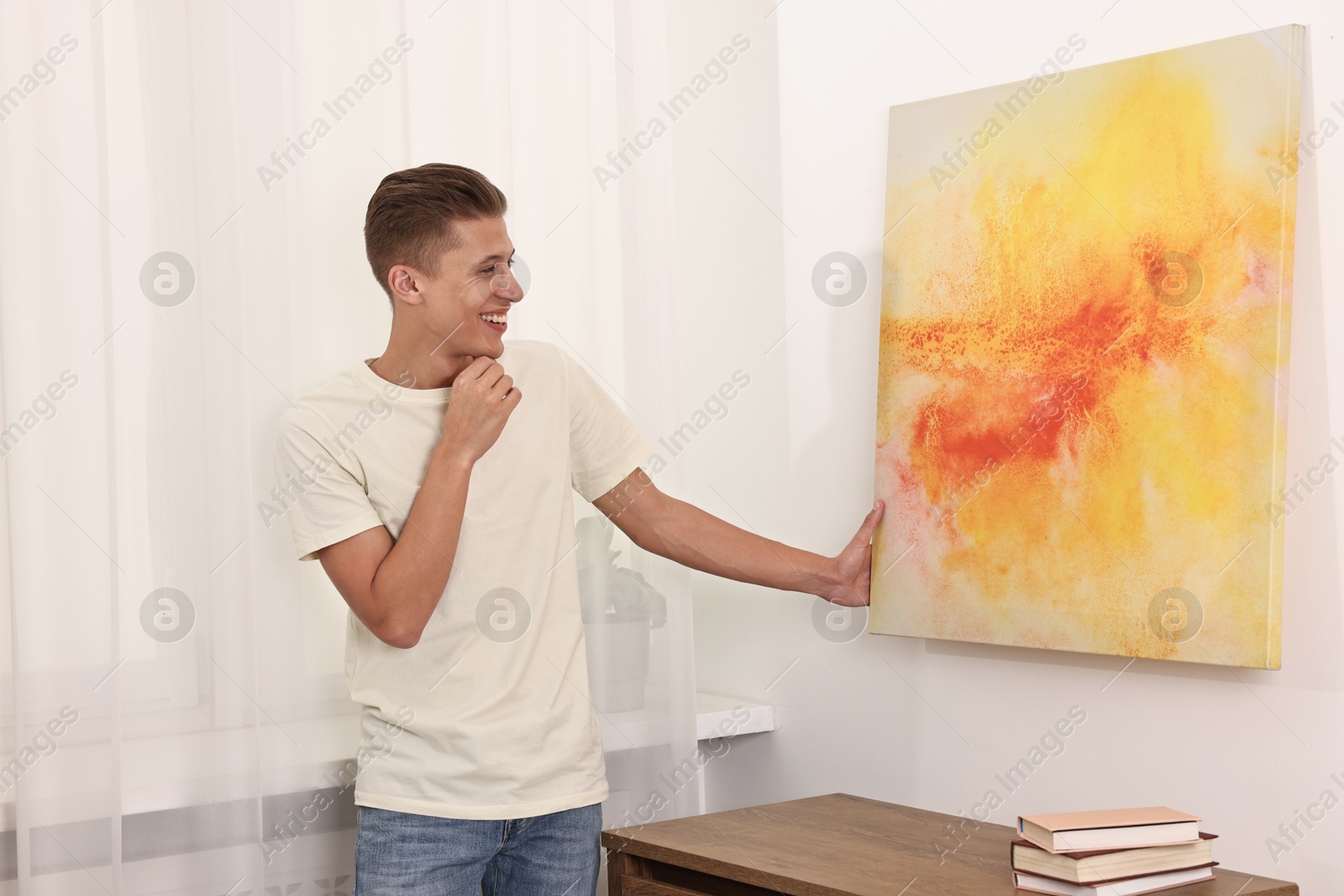 Photo of Smiling young decorator hanging abstract picture indoors