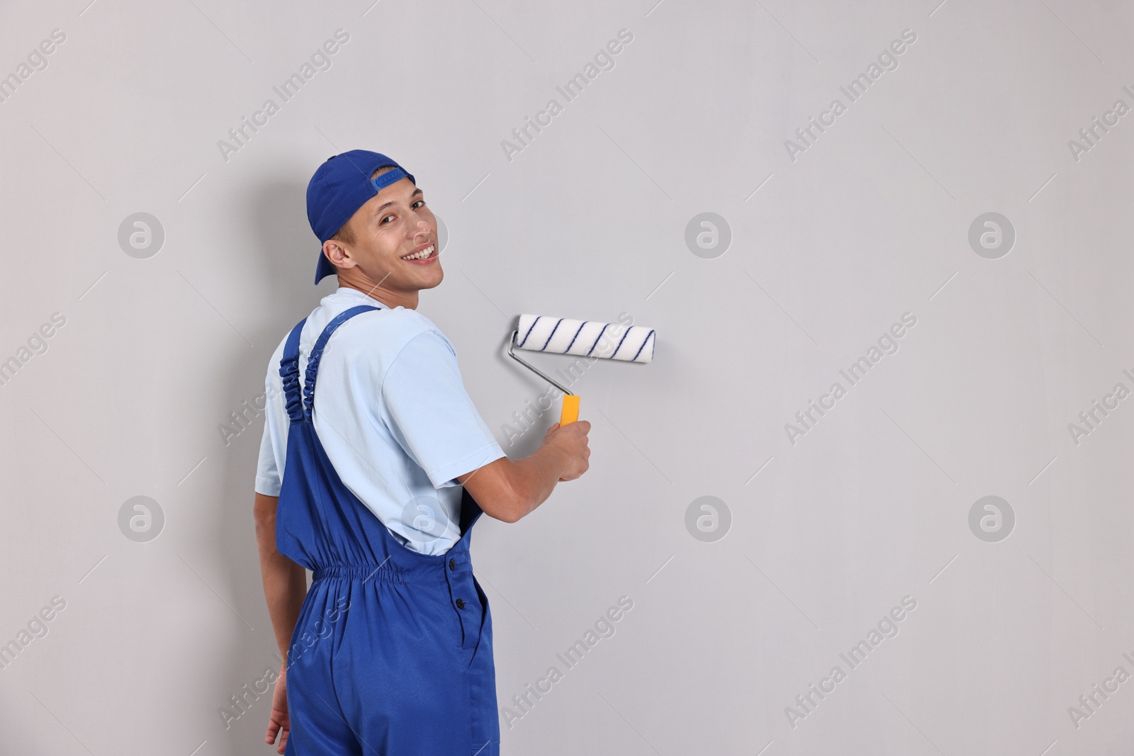 Photo of Smiling handyman painting wall with roller indoors. Space for text