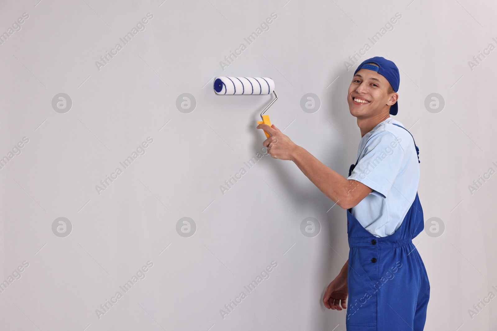 Photo of Smiling handyman painting wall with roller indoors. Space for text