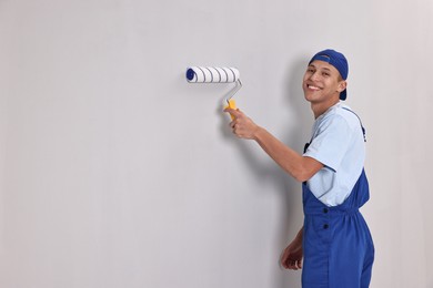 Photo of Smiling handyman painting wall with roller indoors. Space for text