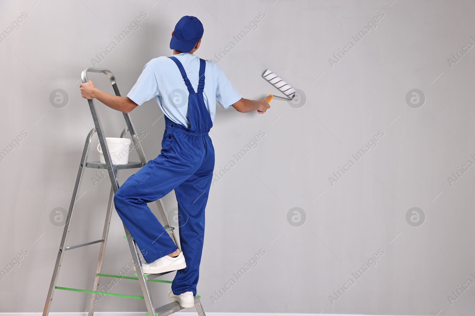 Photo of Male handyman painting wall with roller indoors, back view. Space for text