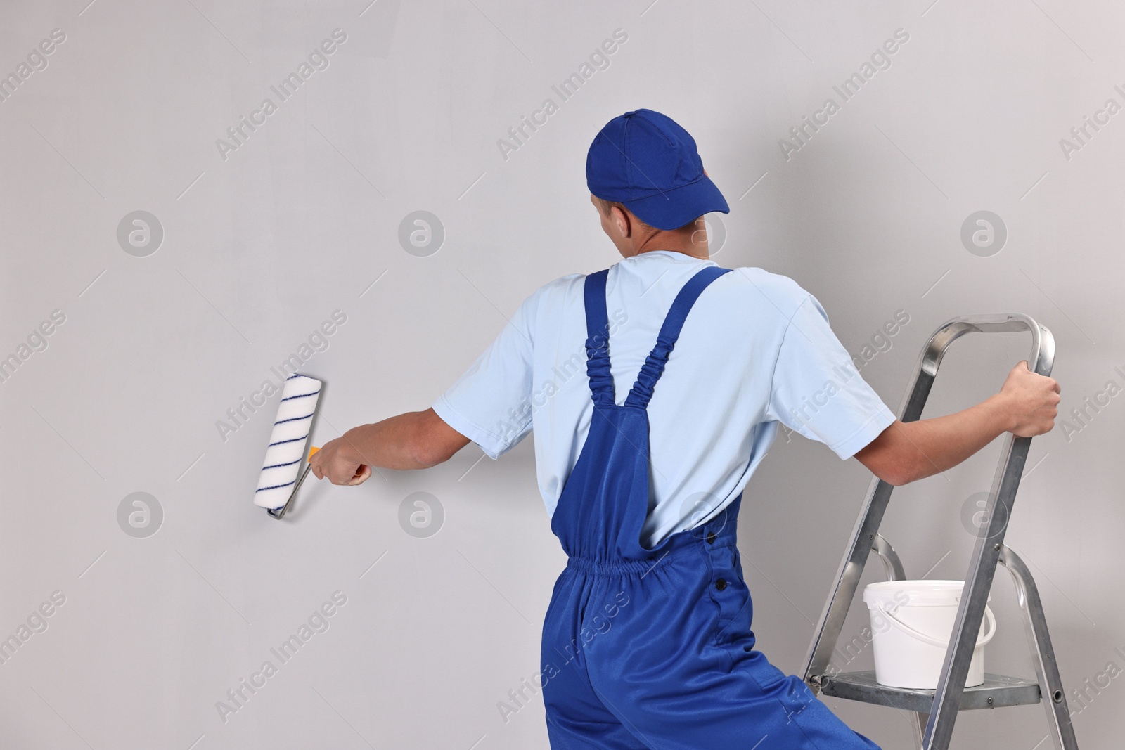 Photo of Male handyman painting wall with roller indoors, back view