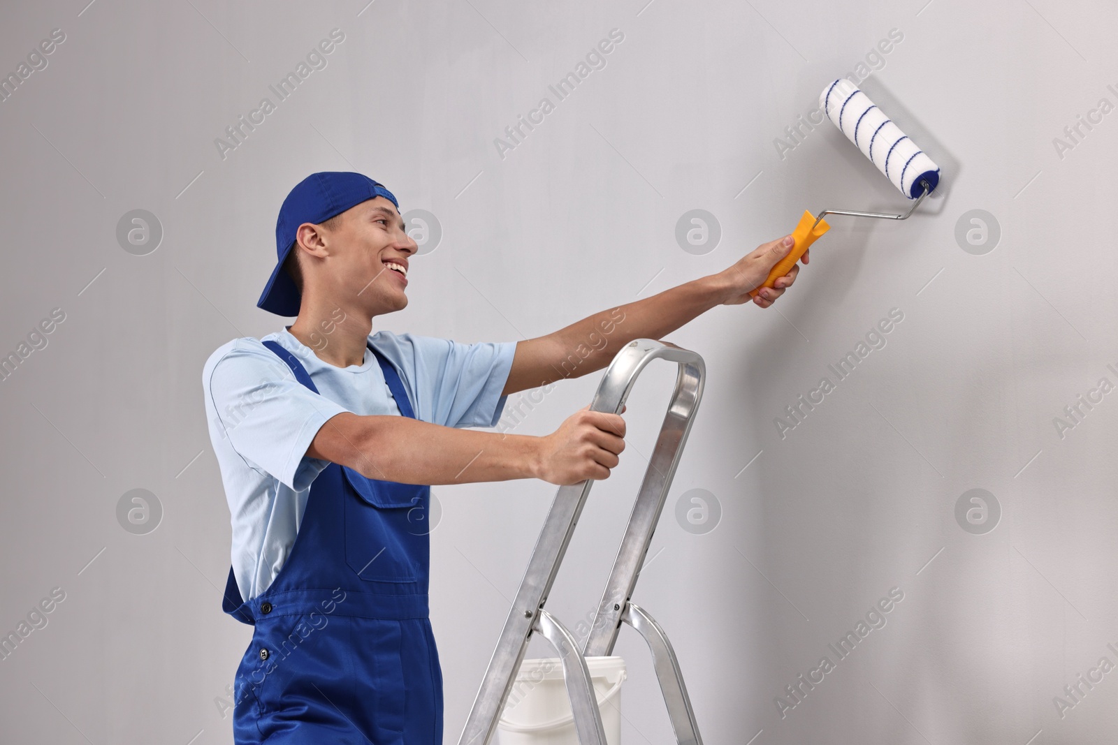 Photo of Smiling handyman painting wall with roller indoors