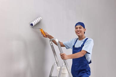 Photo of Smiling handyman painting wall with roller indoors