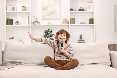 Photo of Little boy with microphone singing on sofa at home