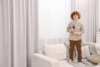 Photo of Little boy with microphone on sofa at home, space for text