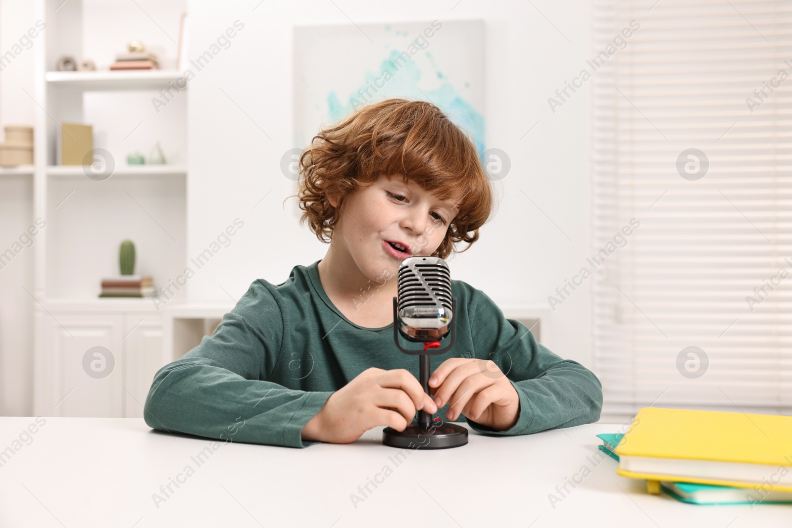 Photo of Little boy with microphone at white table indoors