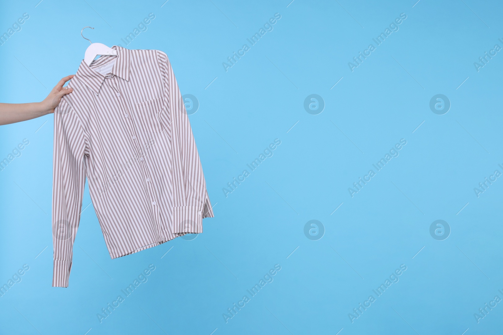 Photo of Woman holding hanger with grey shirt on light blue background, closeup. Space for text