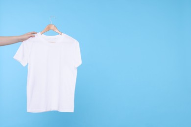 Photo of Woman holding hanger with white t-shirt on light blue background, closeup. Space for text