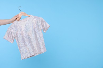 Photo of Woman holding hanger with grey t-shirt on light blue background, closeup. Space for text