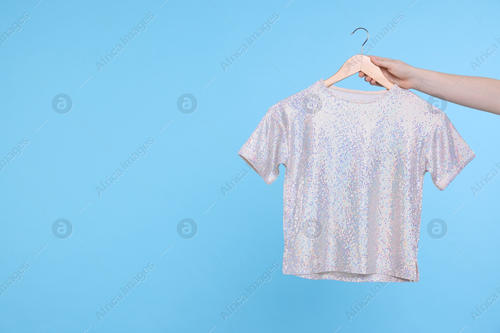 Photo of Woman holding hanger with grey t-shirt on light blue background, closeup. Space for text