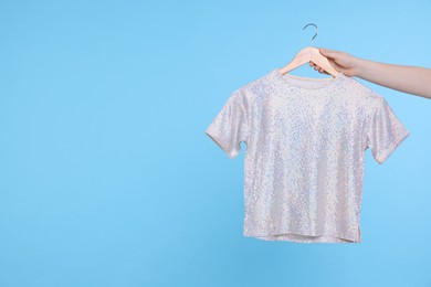 Photo of Woman holding hanger with grey t-shirt on light blue background, closeup. Space for text