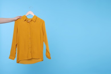 Photo of Woman holding hanger with orange shirt on light blue background, closeup. Space for text