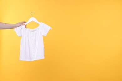 Photo of Woman holding hanger with white t-shirt on yellow background, closeup. Space for text