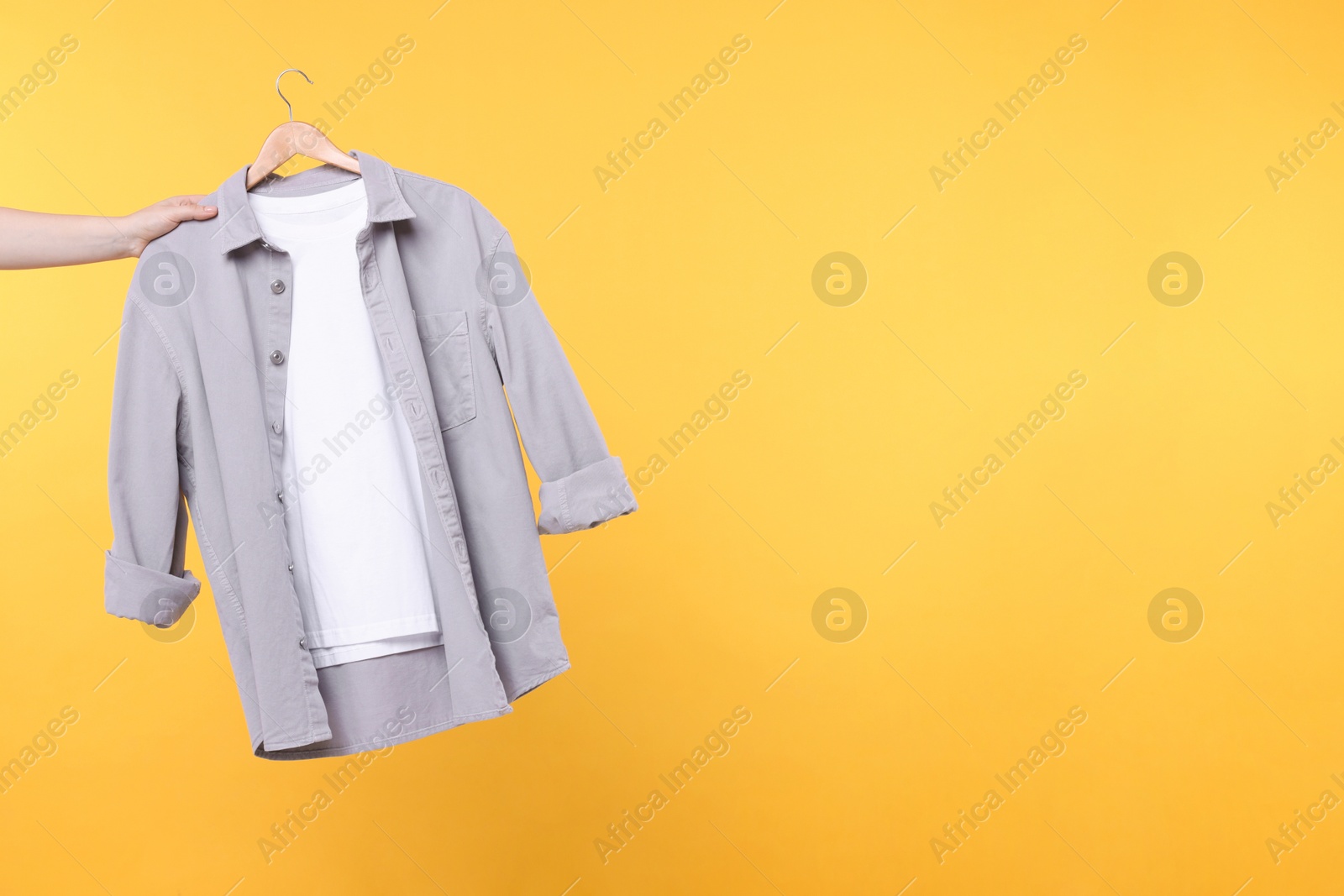 Photo of Woman holding hanger with clothes on yellow background, closeup. Space for text