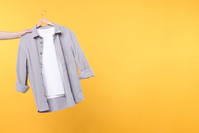 Photo of Woman holding hanger with clothes on yellow background, closeup. Space for text