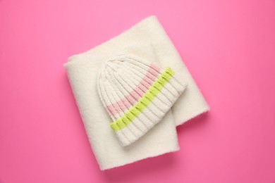 Photo of Warm woolen hat and scarf on pink background, top view