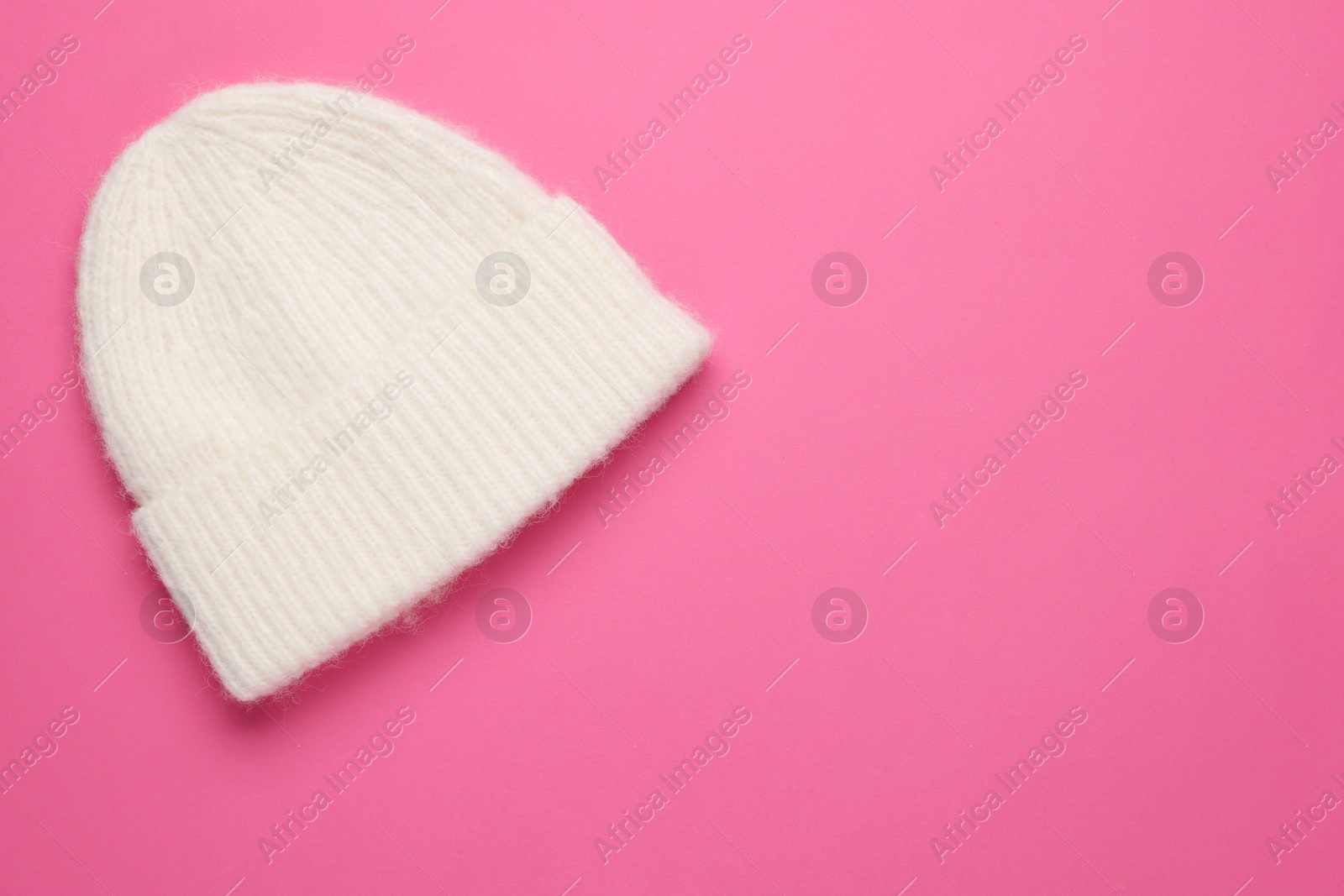 Photo of Warm woolen hat on pink background, top view. Space for text