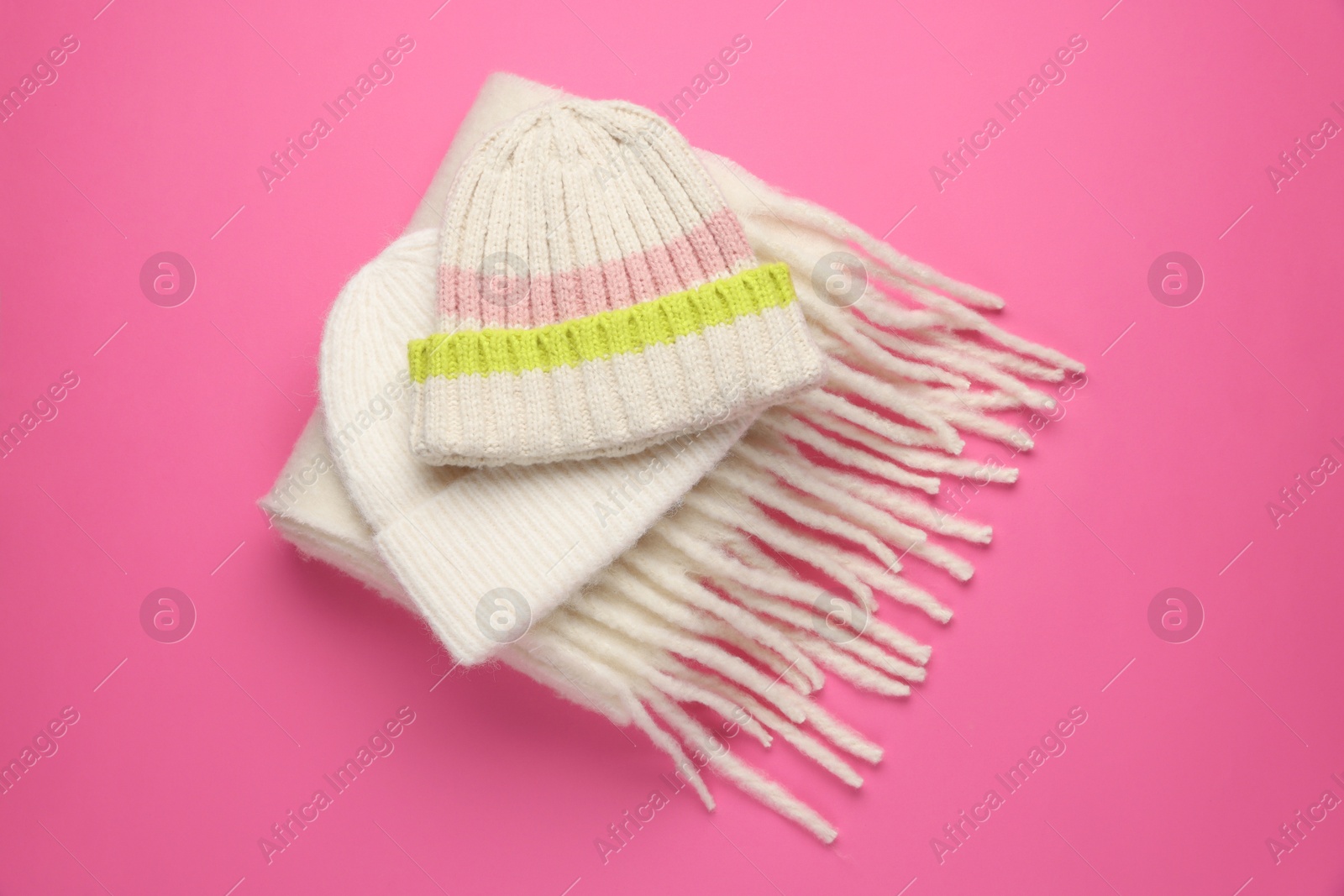 Photo of Warm woolen hats and scarf on pink background, above view