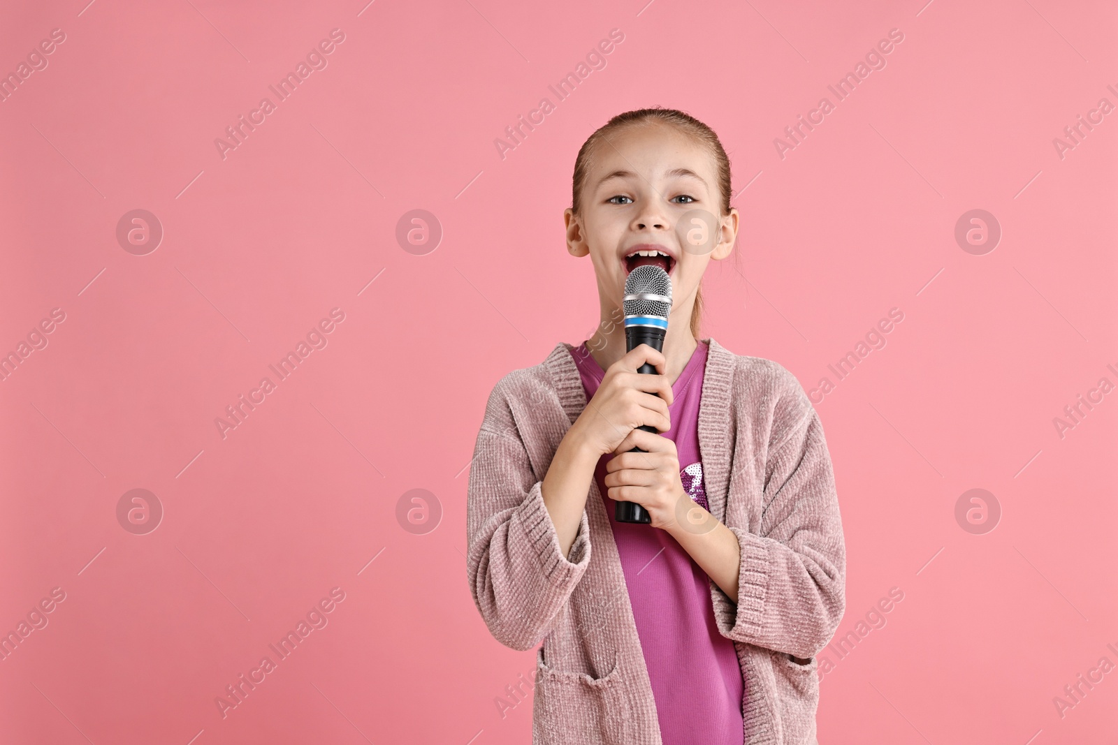 Photo of Little girl with microphone singing on pink background