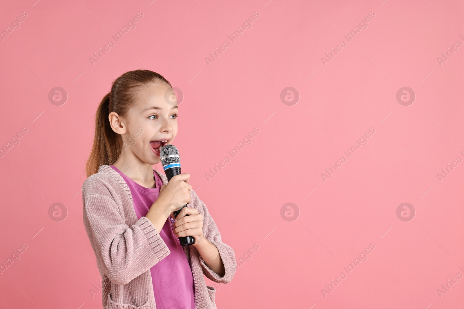 Photo of Little girl with microphone singing on pink background, space for text