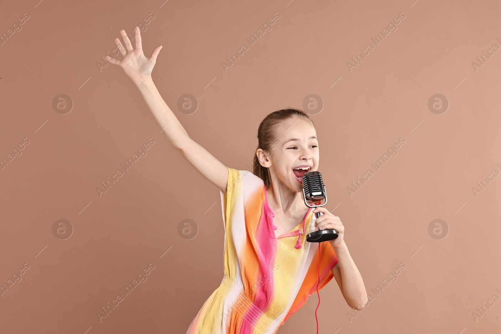 Photo of Little girl with microphone singing on light brown background