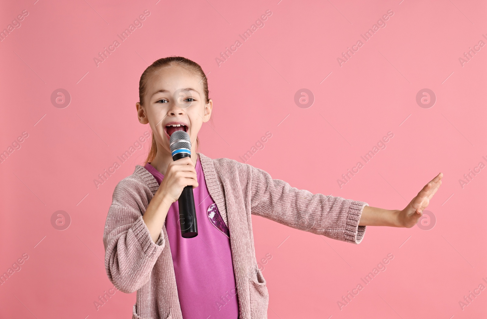 Photo of Little girl with microphone singing on pink background