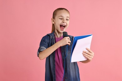 Photo of Little girl with microphone and notebook singing on pink background