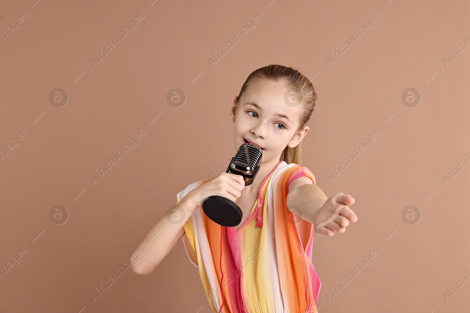 Photo of Little girl with microphone singing on light brown background