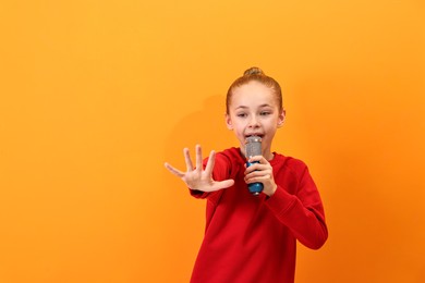 Photo of Little girl with microphone singing on orange background, space for text