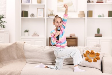 Photo of Little girl with microphone singing on sofa at home