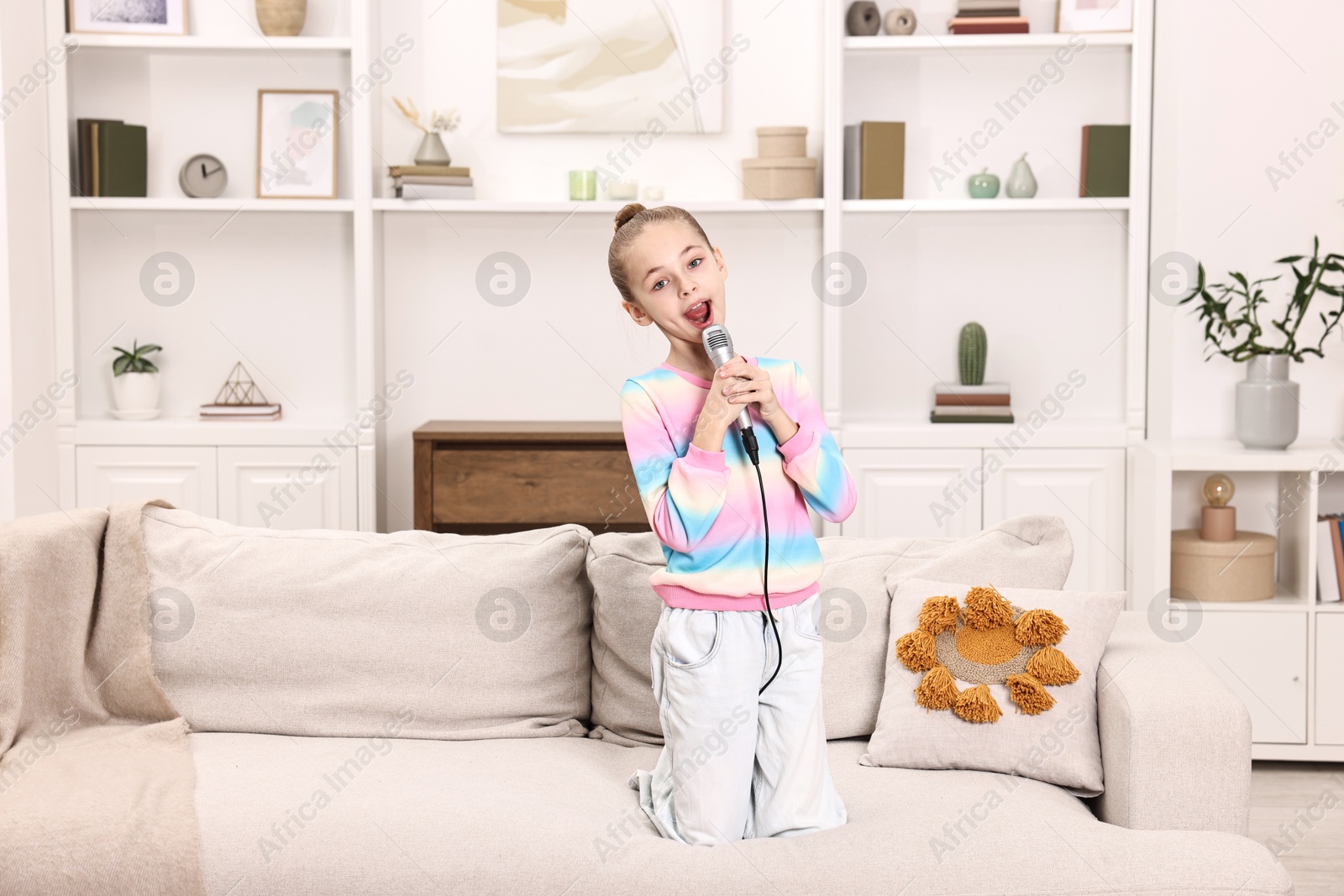 Photo of Little girl with microphone singing on sofa at home