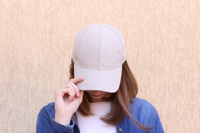 Photo of Woman in stylish baseball cap near beige wall. Mockup for design