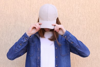 Photo of Woman in stylish baseball cap near beige wall. Mockup for design