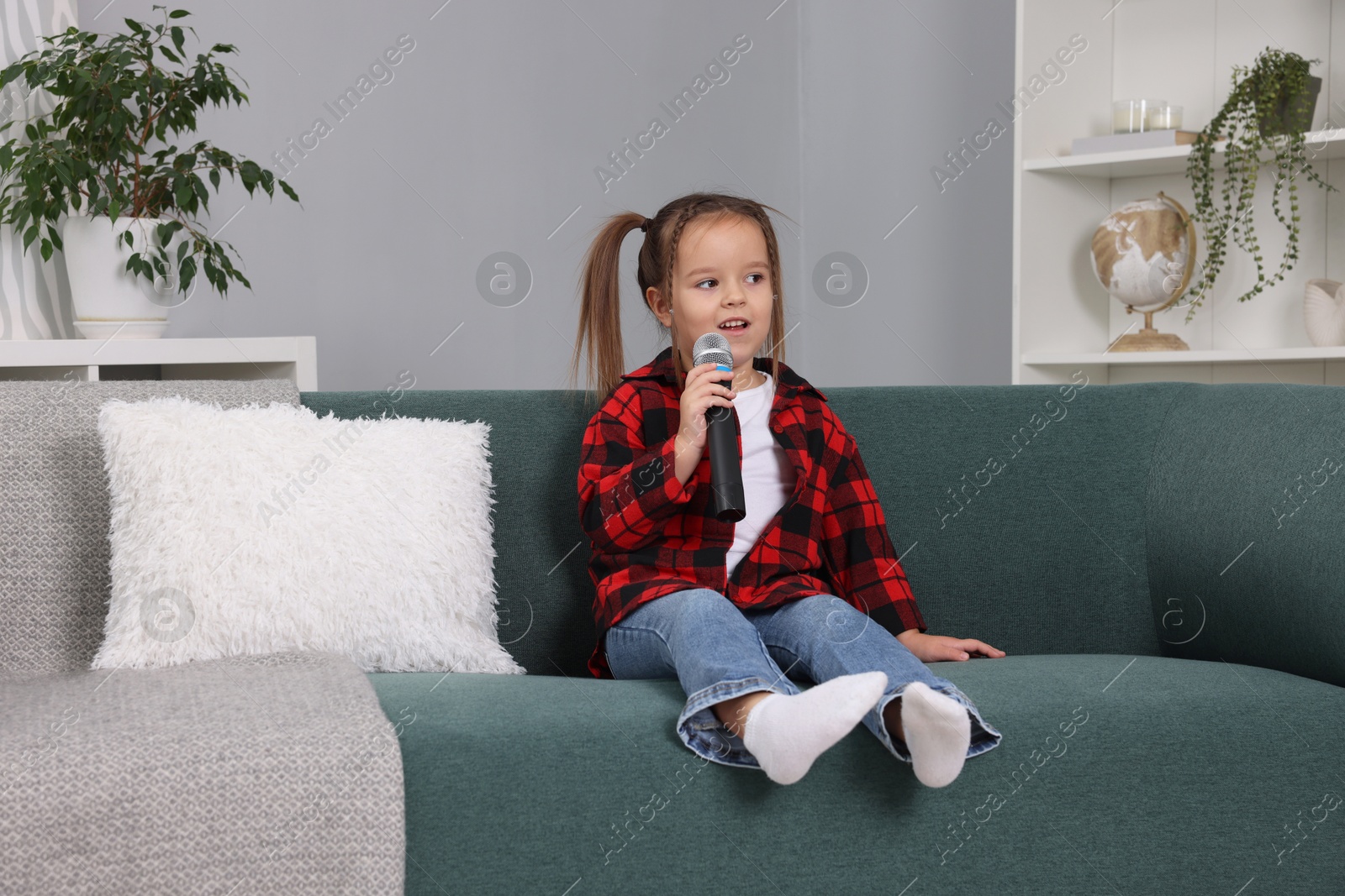 Photo of Cute girl with microphone singing on sofa at home