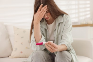 Photo of Upset woman with negative pregnancy test on sofa at home, selective focus